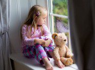 child sitting with her teddy bear looking out the window